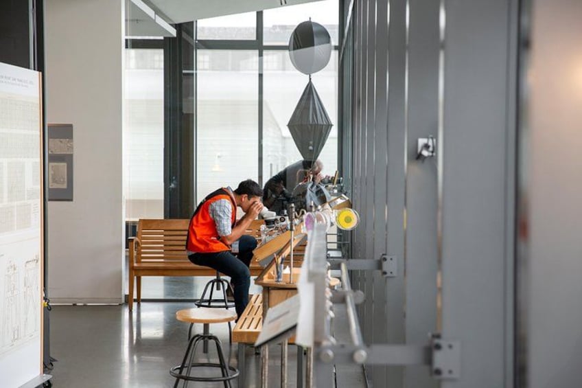 Two people working at a desk with a laptop, a chair, and a window in the background. 2