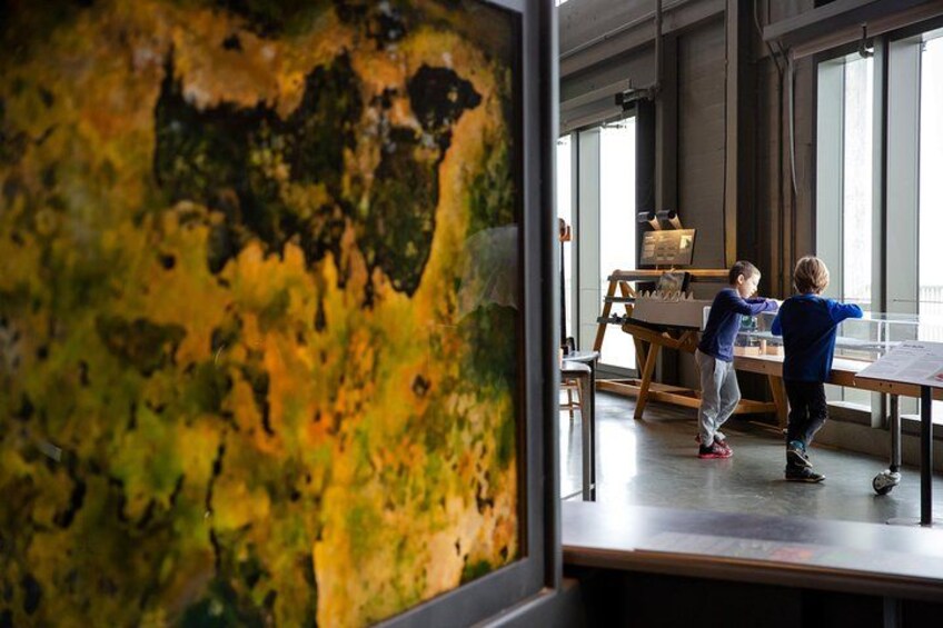 Two children playing at a table in a room with large windows and a textured wall. 3