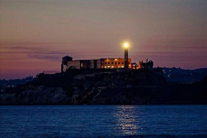 Una fortificación costera al atardecer con una torre destacada y ventanas iluminadas. 2