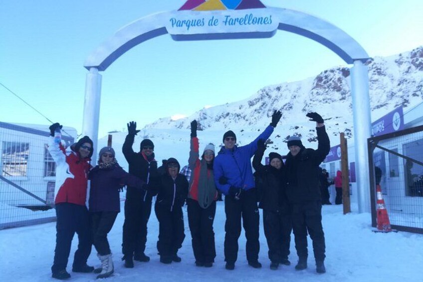 A group of people posing in front of a sign that reads 'Parques de Farellones' with snow-covered mountains in the background. 2