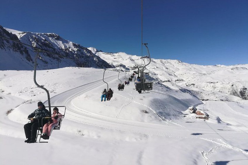 A ski lift in a snowy mountainous area with skiers and snowboarders. 1