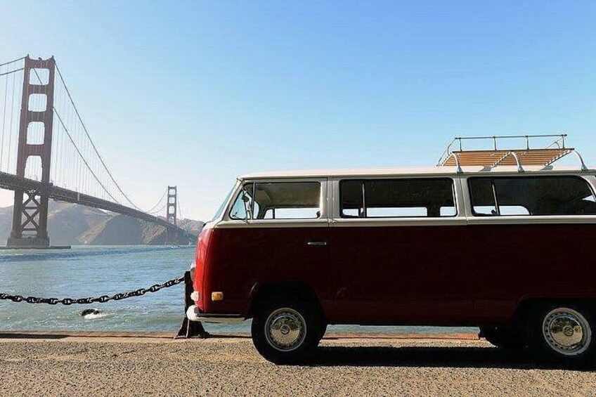A red van parked by a body of water with a large bridge in the background. 2