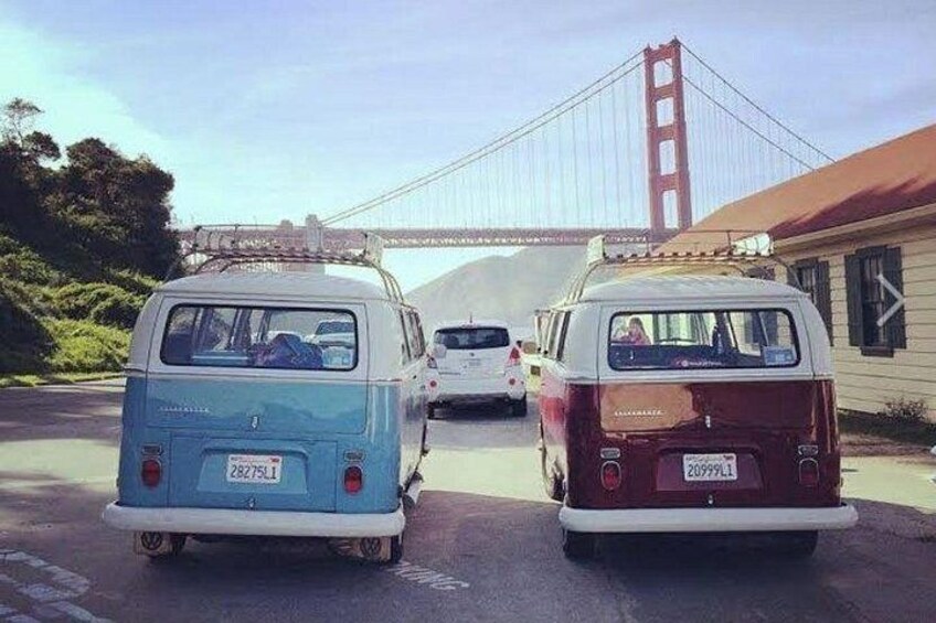 Two vintage vans parked on a street with a bridge in the background. 3