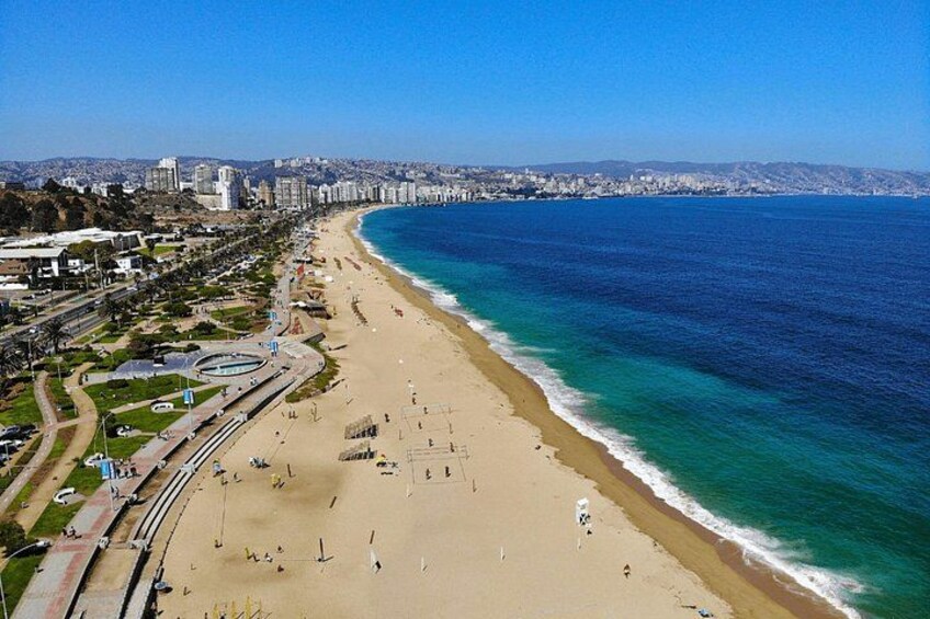 A coastal cityscape with a wide beach, a clear blue sea, and a distant city skyline. 2