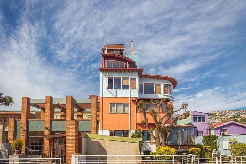 A multi-story building with a curved roof, surrounded by a fence and various plants. 5