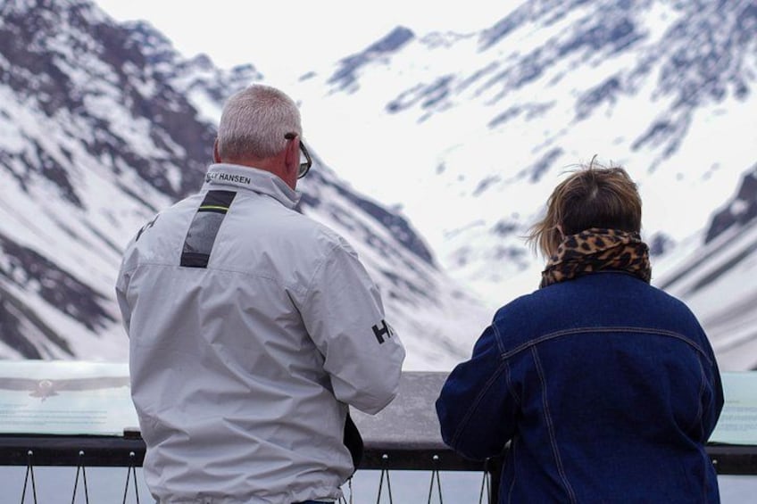To personer står ved et gelænder og ser ud over et snækkedækket bjerglandskab. 4