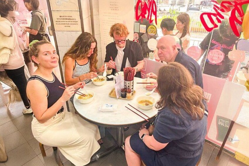 A group of people dining at a restaurant with a round table, chopsticks, and bowls of food. 2