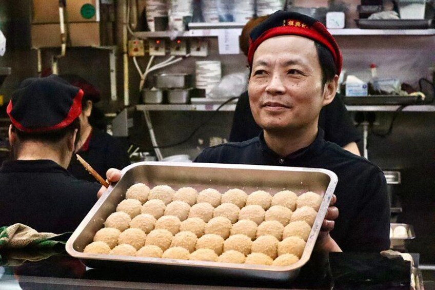 A person holding a tray of round, golden-brown pastries in a kitchen setting. 5