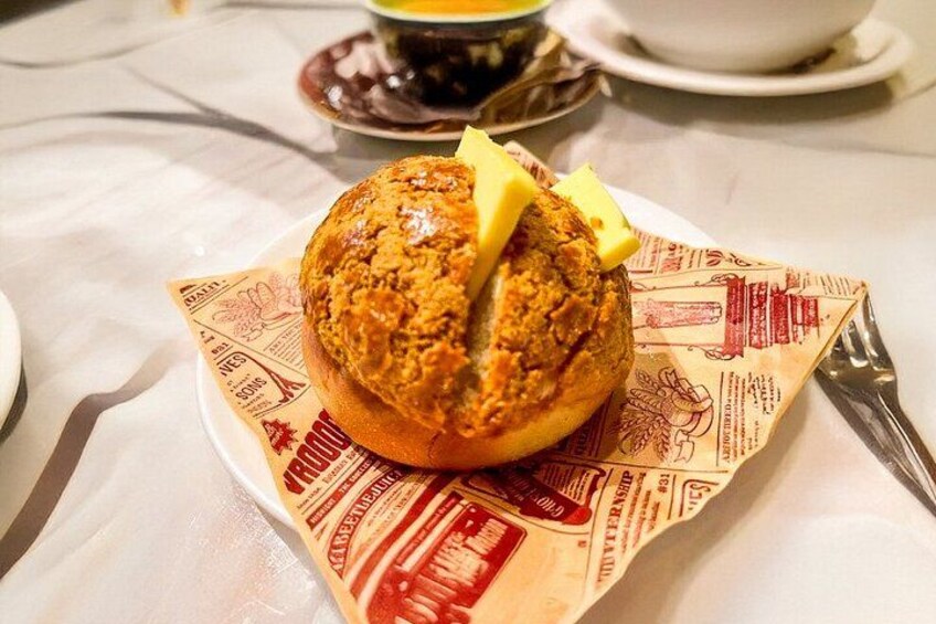 A muffin with a pat of butter on a paper plate with a newspaper print. 2