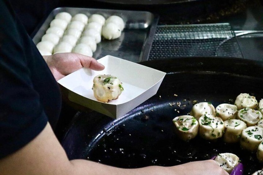 A person holding a dumpling in a white box, with more dumplings on a black tray. 4
