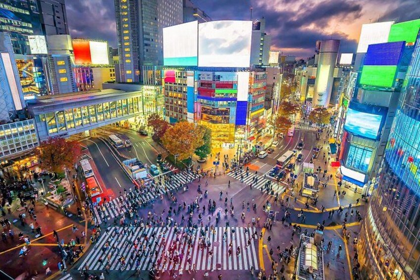 A busy urban intersection with tall buildings and illuminated billboards. 2