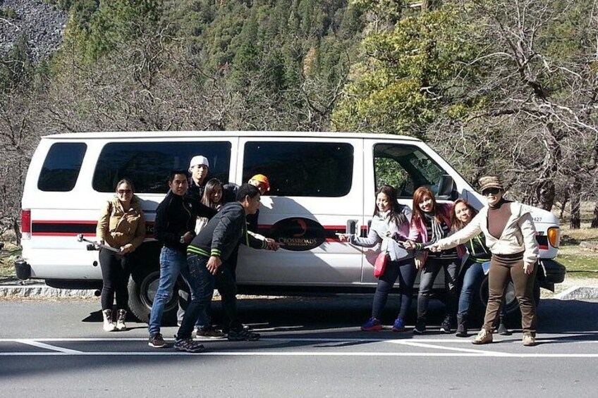 A group of people standing around a white van on a road with trees in the background. 2