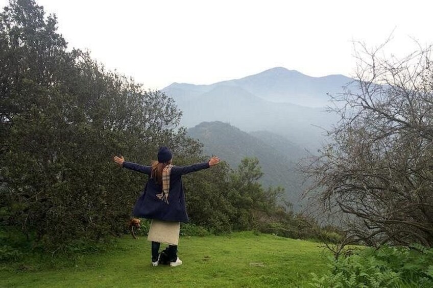Une personne se tient debout sur une colline herbeuse, les bras tendus, face à un paysage montagneux. 1