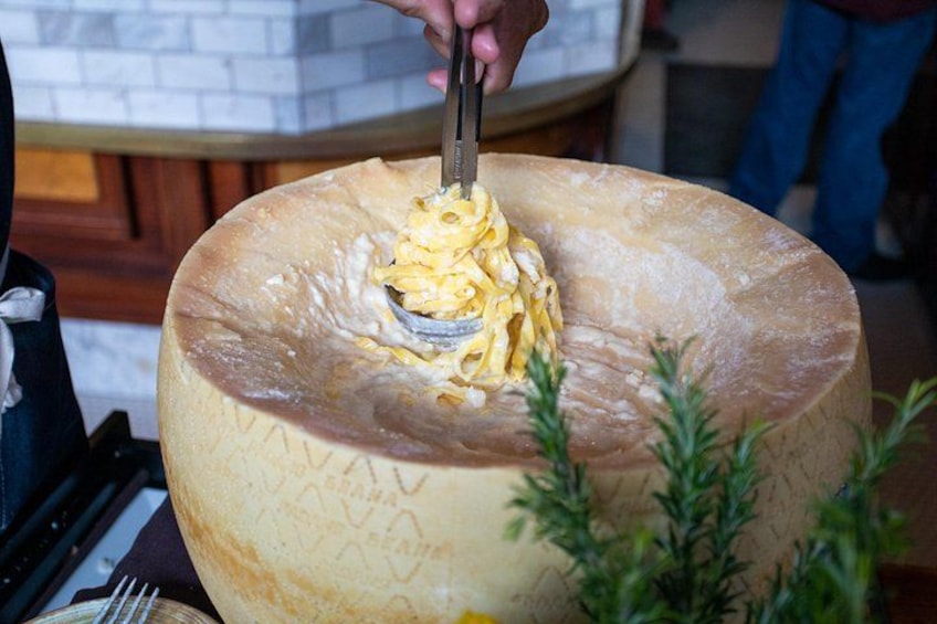 A person cutting into a large, round, wooden serving dish filled with pasta. 2