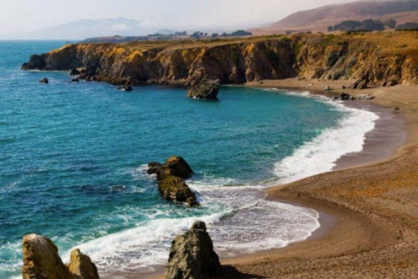 A coastal landscape with a sandy beach, rocky outcrops, and a clear blue ocean. 2