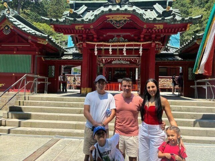 A family in front of a traditional red and green temple with ornate architecture. 1