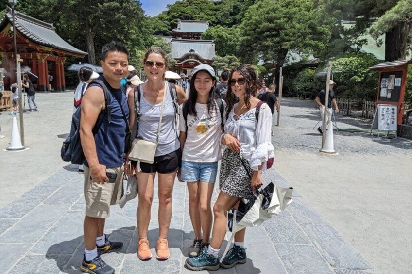 En gruppe mennesker poserer foran en traditionel japansk tempel med stenhinner og røde torii-porte. 5