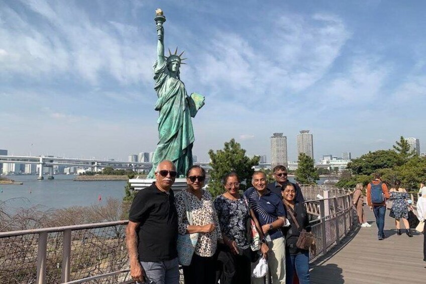 Un groupe de personnes posant devant la Statue de la Liberté, avec une rivière et un pont en arrière-plan. 4