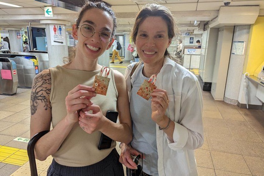Two people holding slices of pizza in a public indoor space with tiled floors and metal barriers. 4