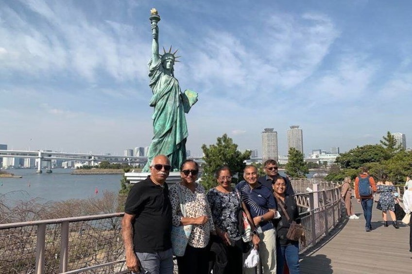 A group of people posing in front of the Statue of Liberty, with a river and city skyline in the background. 3