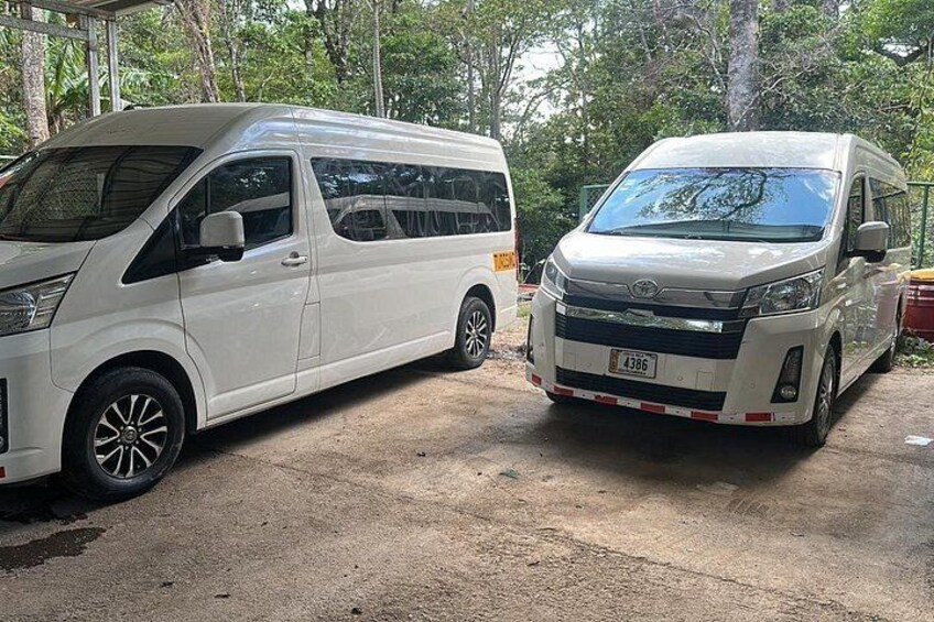 Two white vans parked on a concrete surface with trees in the background. 4