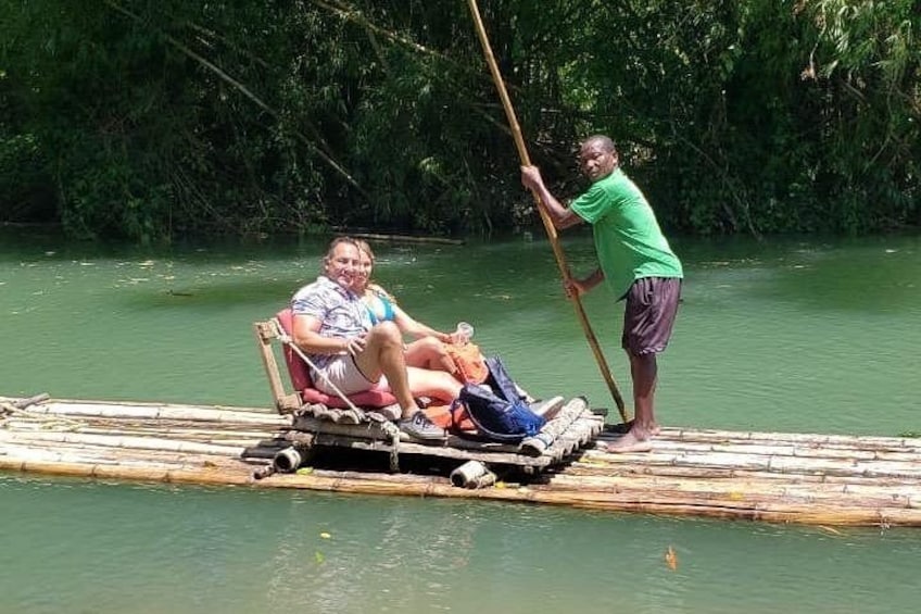 A person standing on a bamboo raft in a river, another person seated on a chair, and a third person standing with a pole. 4