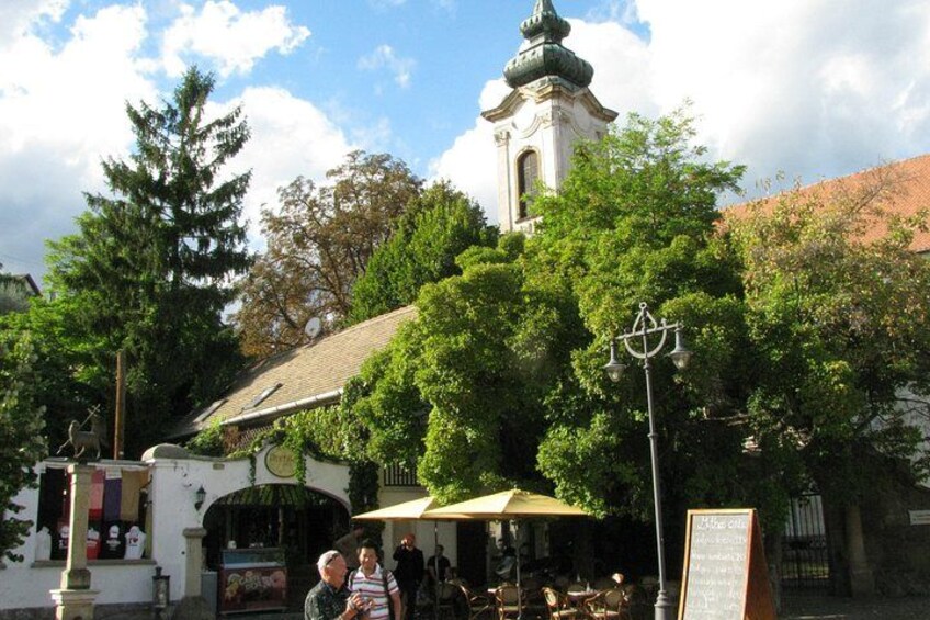 A town square with a clock tower, a café, and people walking. 5