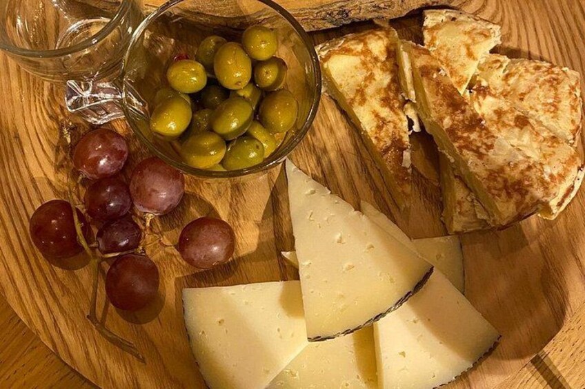 A wooden cutting board with cheese, grapes, olives, and a glass pitcher. 3