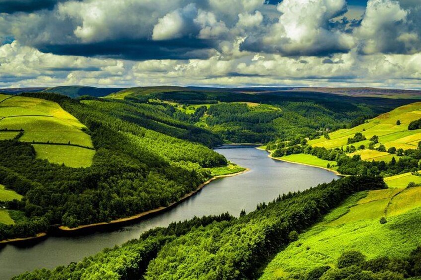 Ein Fluss schlängelt sich durch ein grünes Tal mit Hügeln und einem bewölkten Himmel. 3