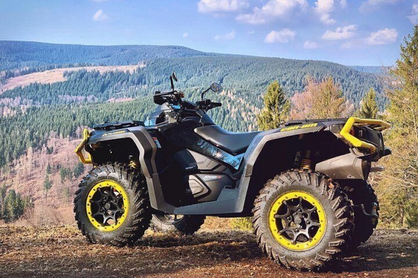 En firhjulet quadbike på en jordvej med skovklædte bjerge i baggrunden. 1