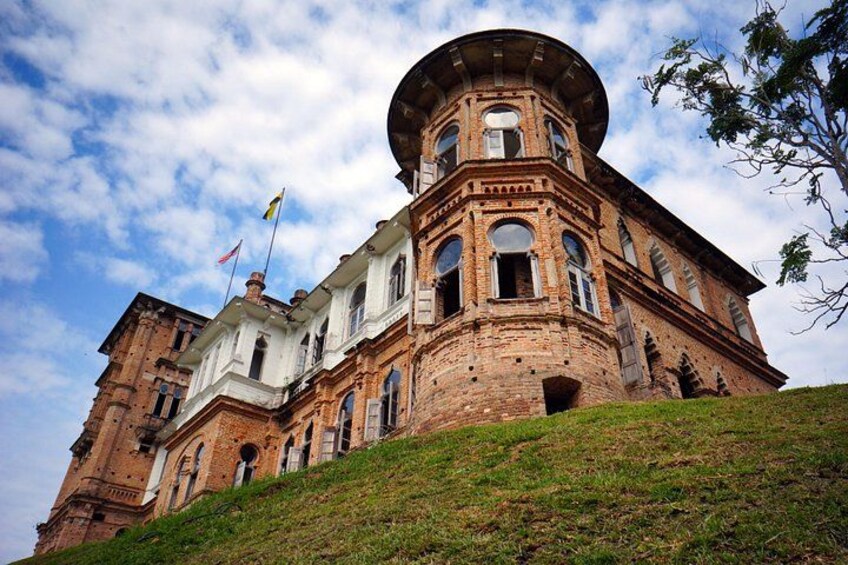 A large, historic brick building with a round tower, surrounded by a grassy hill. 4