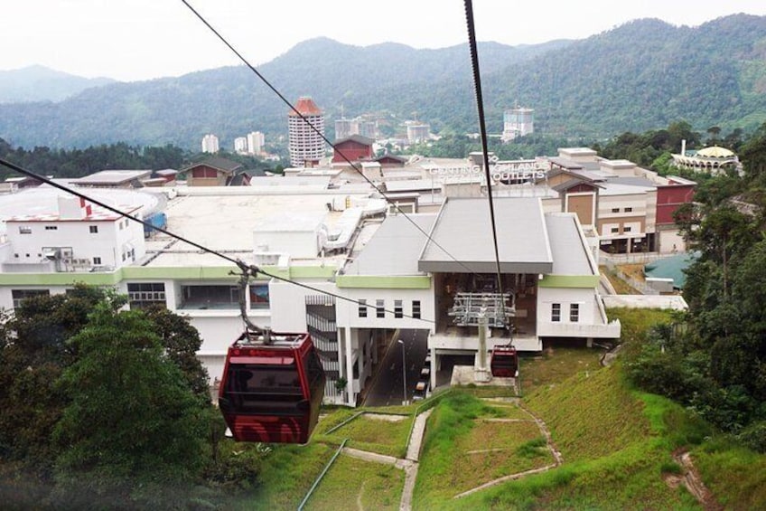 A cable car system with a red cable car in motion, a building with a sign reading "TRAINING PLANT & TOILETS", and a mountainous landscape in the background. 4