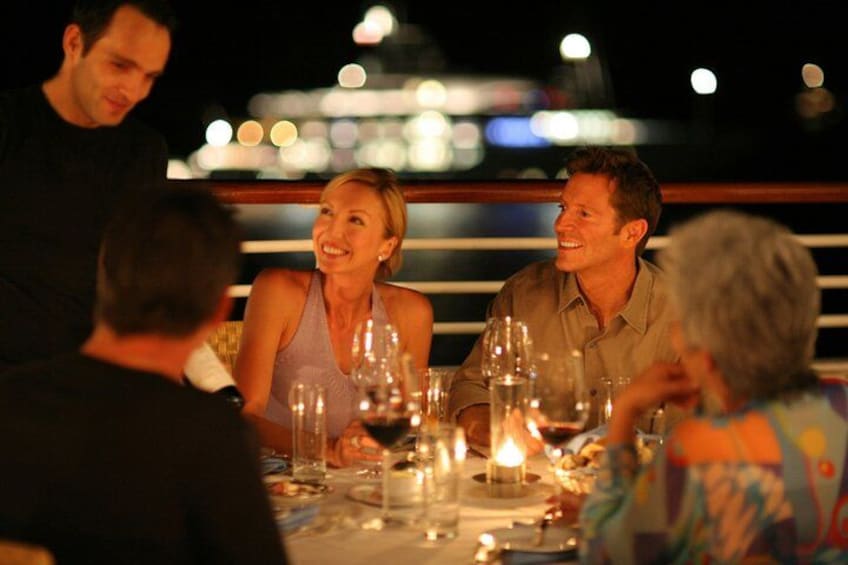A group of people dining at a table with a ship in the background. 1
