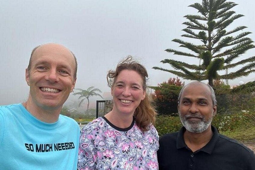 Three people standing outdoors with a large tree and some greenery in the background. 2