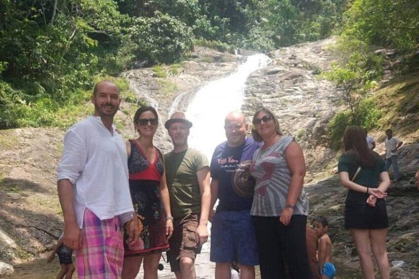 A group of people standing near a waterfall in a forested area. 3