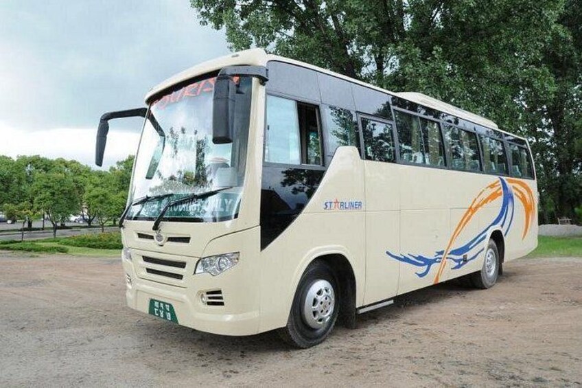 A large, cream-colored bus with blue and orange designs parked on a dirt road. 5
