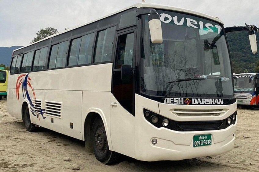 A white bus with 'DESH DARSHAN' branding and 'TOURIST' on the windshield, parked on a sandy surface. 1