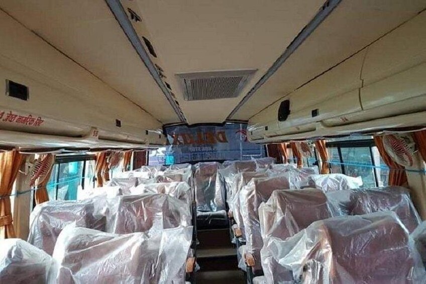 A bus interior with seats covered in plastic, a sign on the ceiling, and curtains on the windows. 2