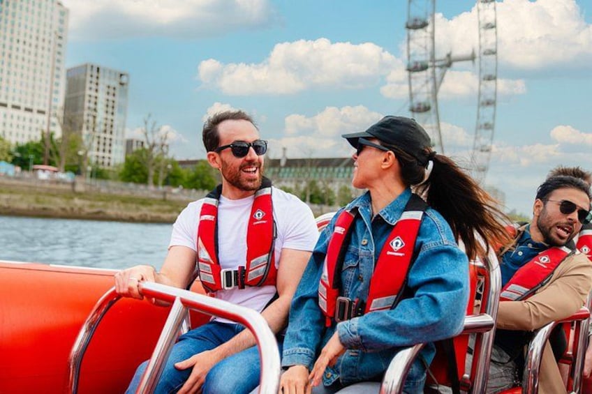 Mensen in een boot met reddingsvesten, met een stadsgezicht en een brug op de achtergrond. 2