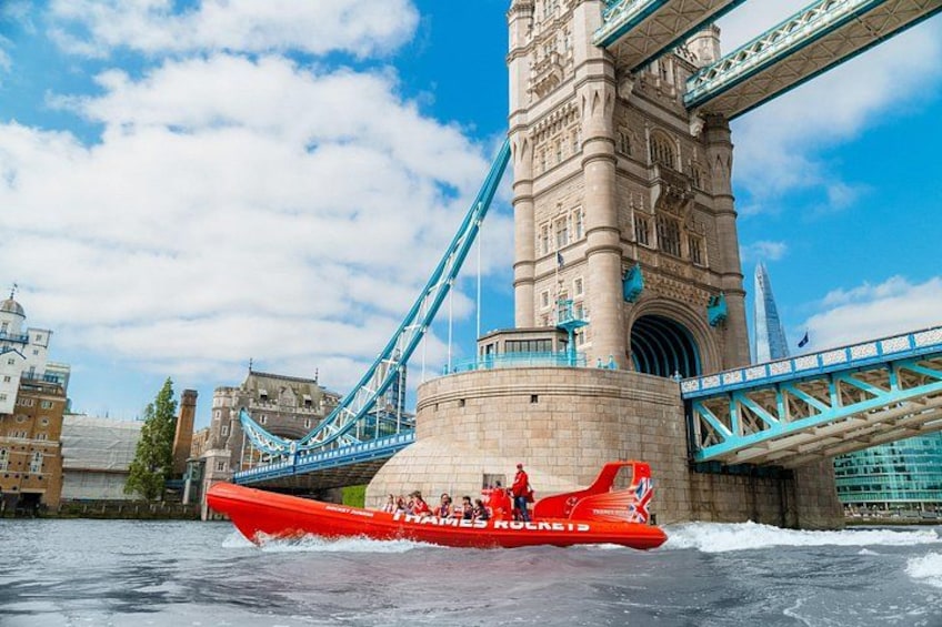 Un bote rojo con pasajeros, un puente y una torre al fondo. 2