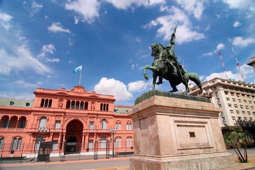 A statue of a man on horseback in front of a pink building with a flag. 2