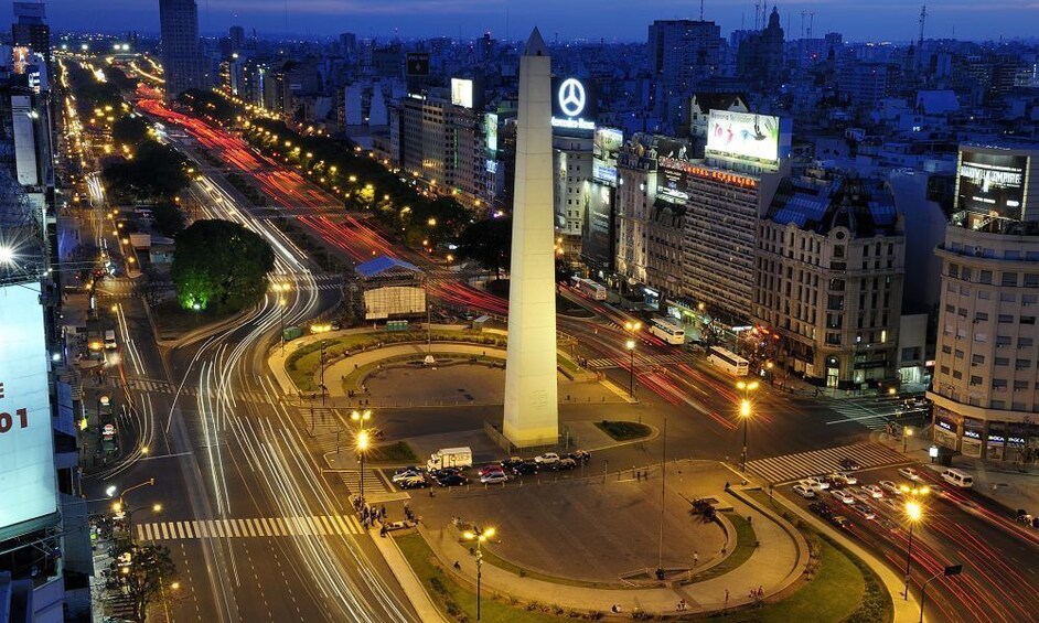 A cityscape at night with a prominent monument, busy roads with light trails, and illuminated buildings. 1