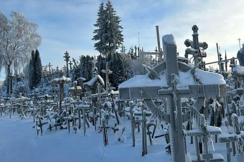 Een besneeuwde begraafplaats met grafstenen en kruisen, omgeven door bomen en een kerk. 5