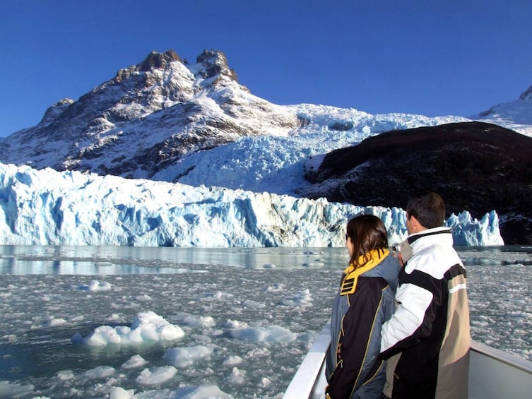 A glacier with a boat in the foreground and a mountain in the background. 1
