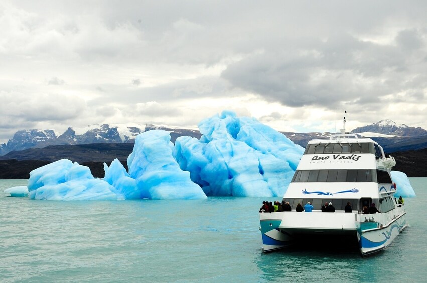 A boat named "Ane Vadis" near large blue icebergs in a body of water with mountains in the background. 2