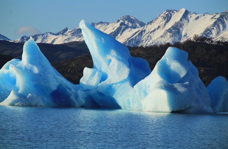 Large blue icebergs in a body of water with snow-covered mountains in the background. 3