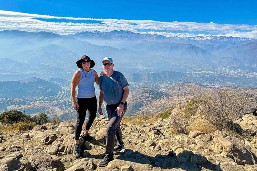 Two people standing on rocky terrain with a mountainous landscape in the background. 1