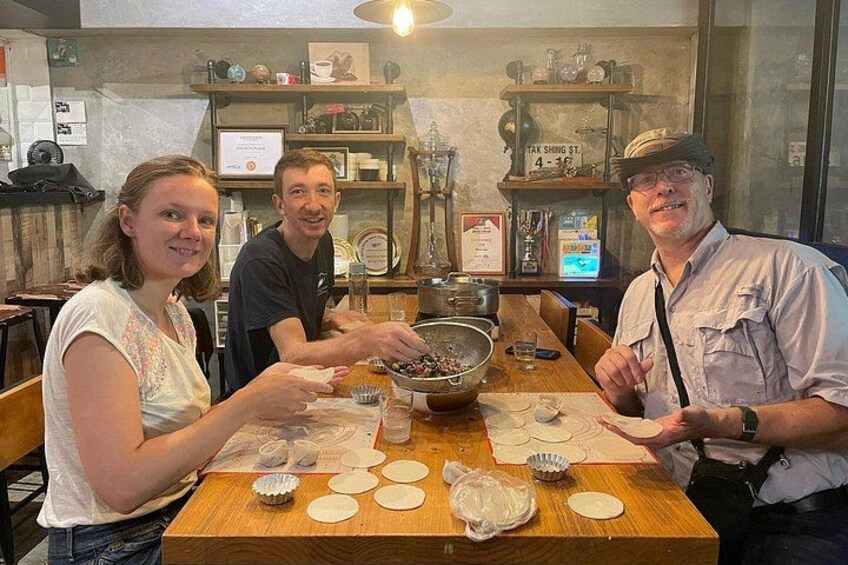 Drie personen aan een houten tafel met deeg en bakgereedschap, in een keuken met planken en een raam. 4