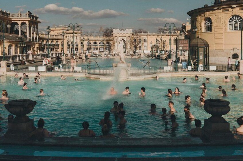A large public swimming pool with people swimming and relaxing, surrounded by classical architecture. 5