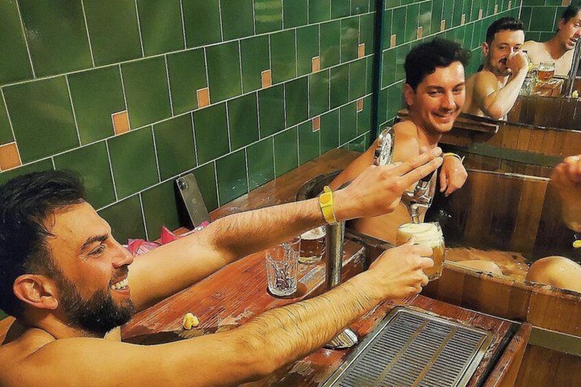 A group of people toasting with drinks at a wooden bar with green tiled walls. 3